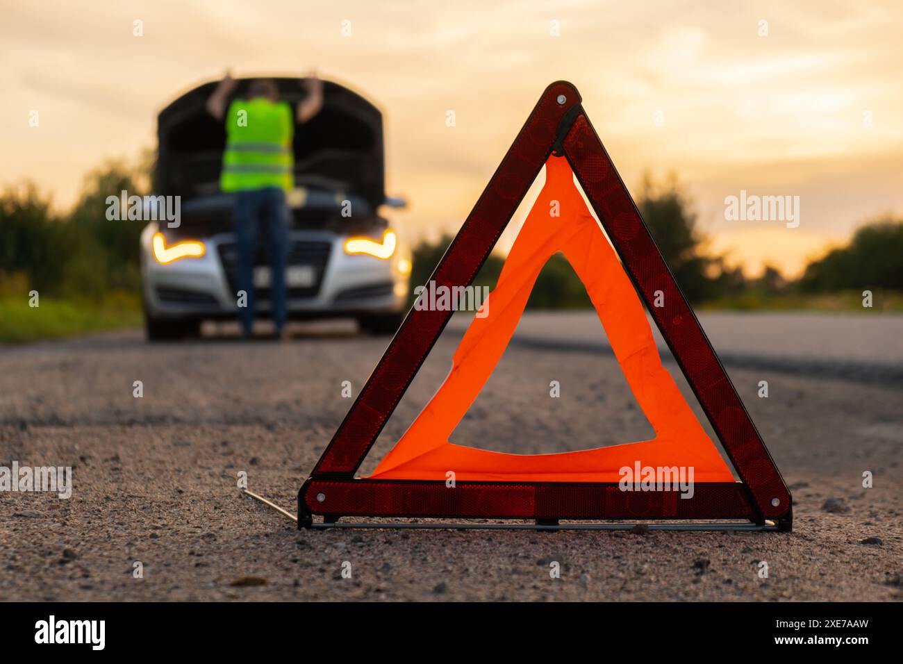 Gebrochenes Silber Luxusauto Notfall Unfall. Man-Fahrer mit rotem Dreieck-Stoppschild auf der Straße. Sportauto eingeschaltet bl Stockfoto