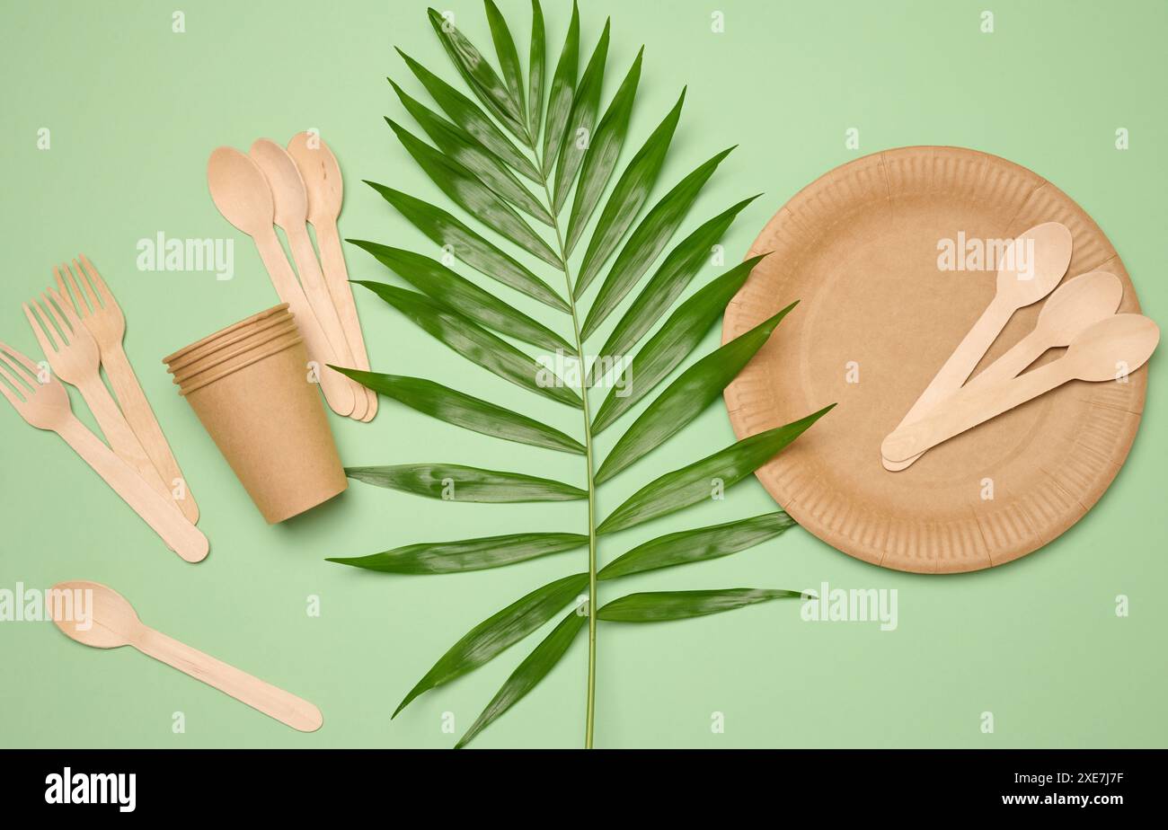 Papierteller und -Tassen, Holzlöffel und Gabeln auf grünem Hintergrund Stockfoto