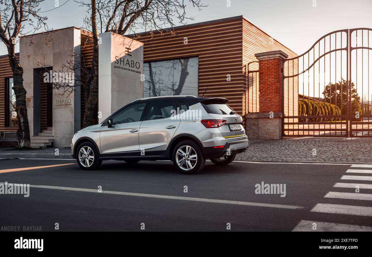 Silver SEAT Arona parkte in der Nähe eines modernen einstöckigen Gebäudes. Dreiviertel-Rückansicht der spanischen Fließheck-Überkreuzung bei Sonnenuntergang. Stockfoto