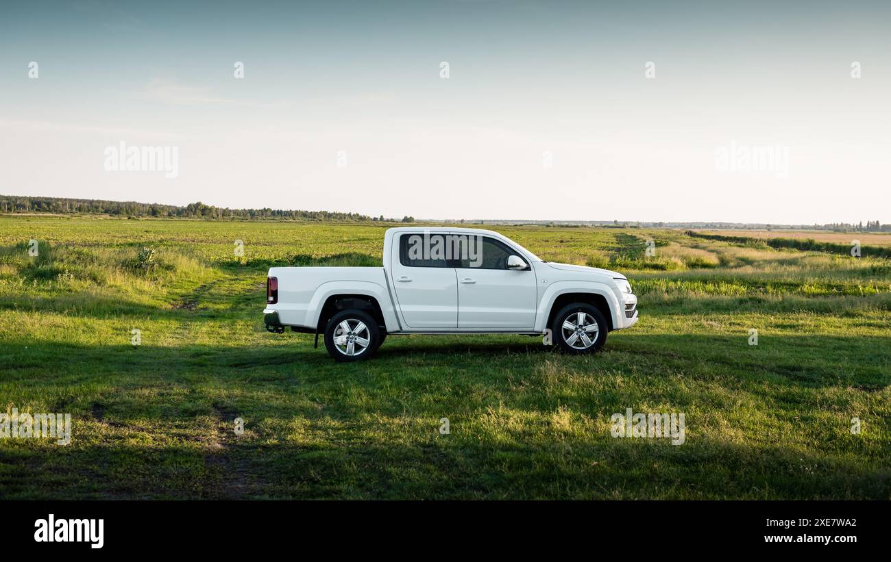 Weißer Volkswagen Amarok auf grüner Wiese. Seitenprofilansicht eines VW-Pickup-Fahrzeugs mit Doppelkabine auf dem Feld. Stockfoto