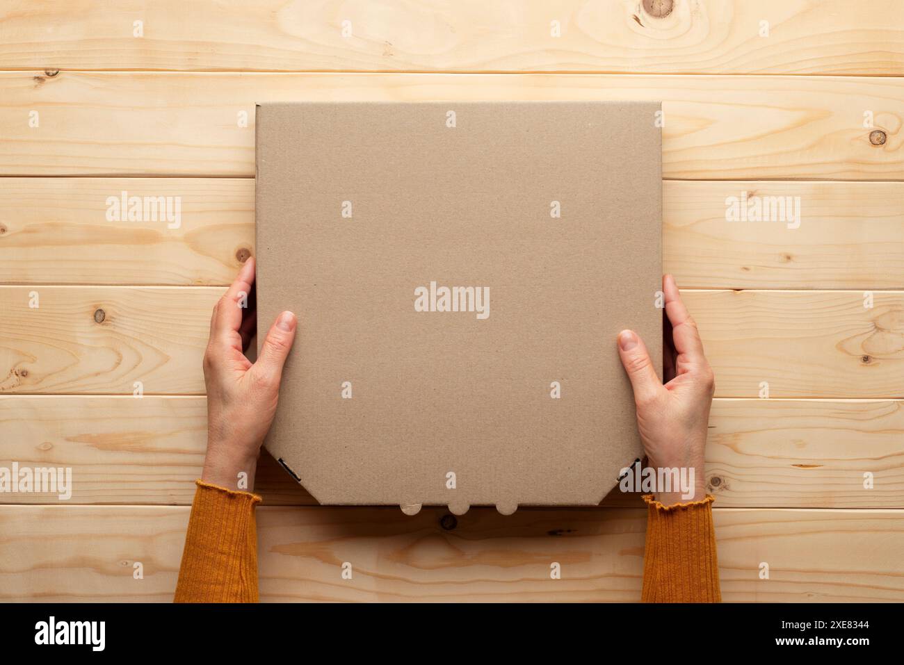 Pizza geschlossener Karton in menschlichen kaukasischen Händen auf natürlichem Holztisch flach liegendes Modell mit Rohling Stockfoto