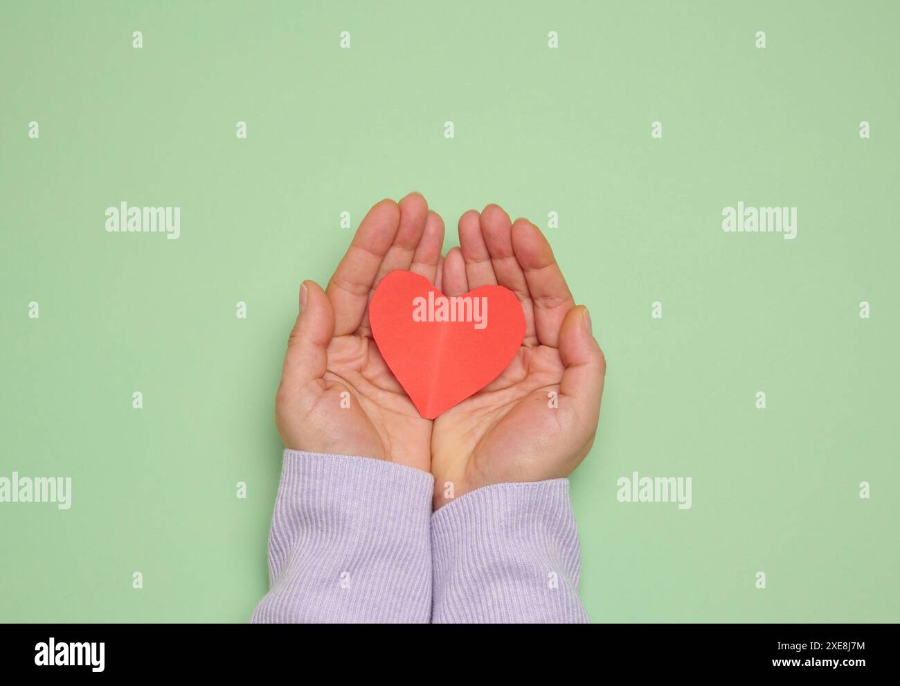 Die Hand einer Frau hält ein rotes Papierherz auf grünem Hintergrund, was das Konzept der Spende symbolisiert Stockfoto