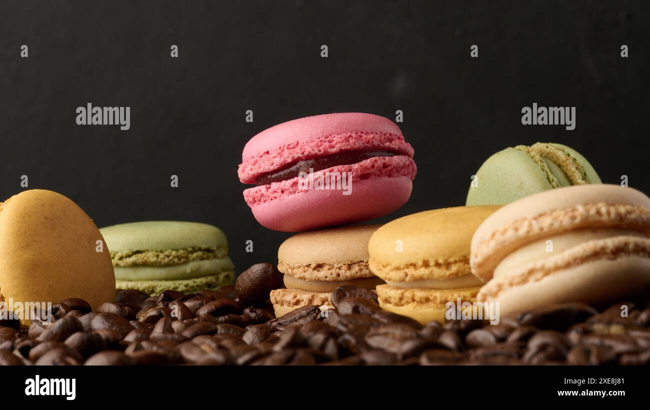 Stapel mehrfarbiger Macarons auf einem Hintergrund aus Kaffeebohnen, schwarzer Hintergrund Stockfoto