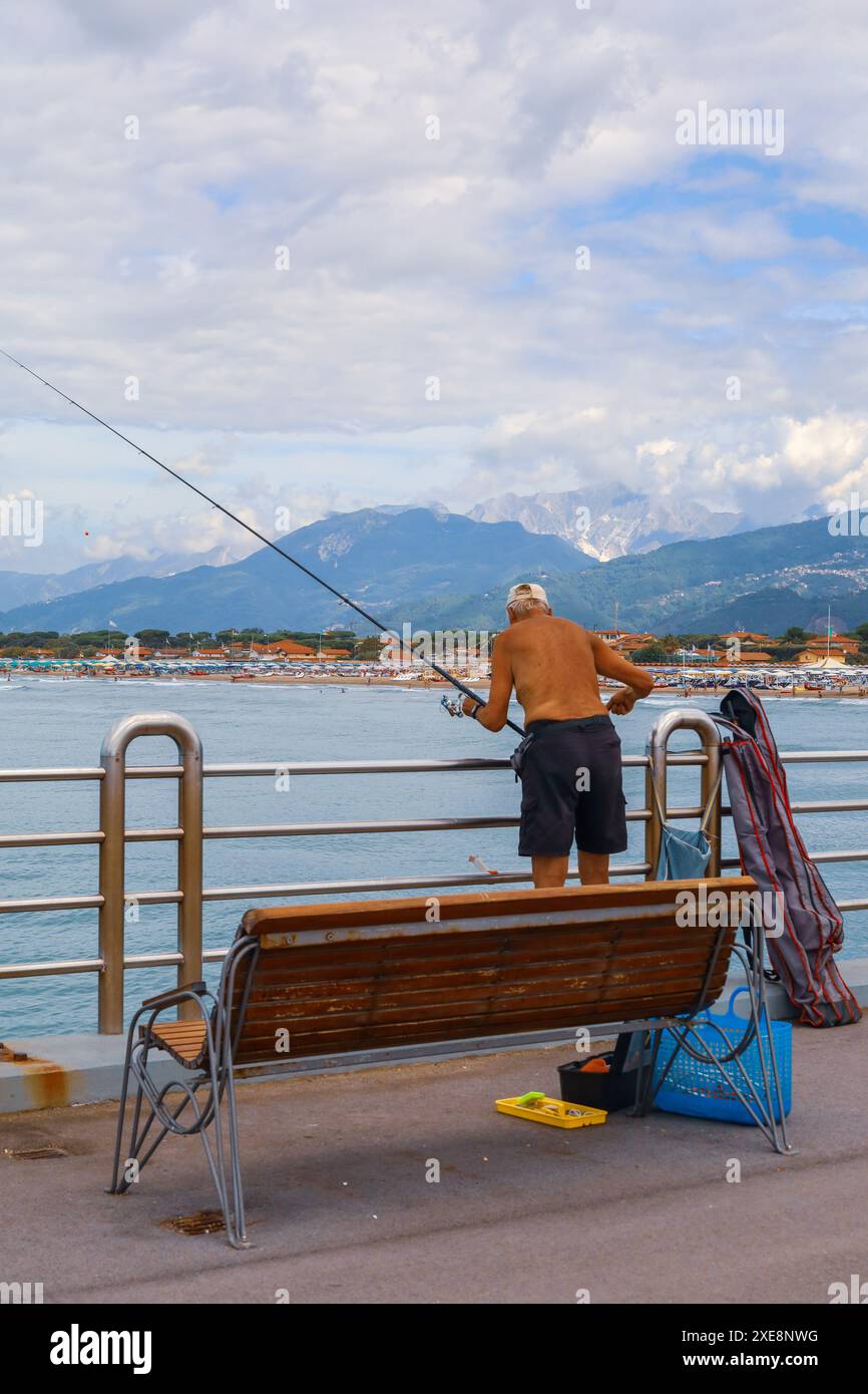Ältere Männer fischen am Pier in Forte dei Marmi Italien. Die Stadt Forte dei Marmi im Hintergrund sowie die Apuanischen Alpen. Stockfoto