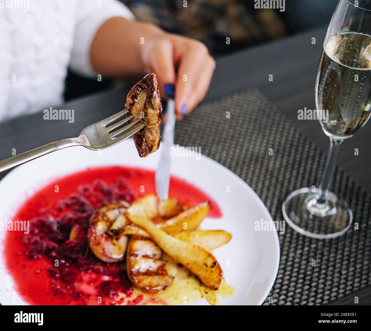 Frau isst Fleisch und trinkt Champagner in einem Restaurant Stockfoto