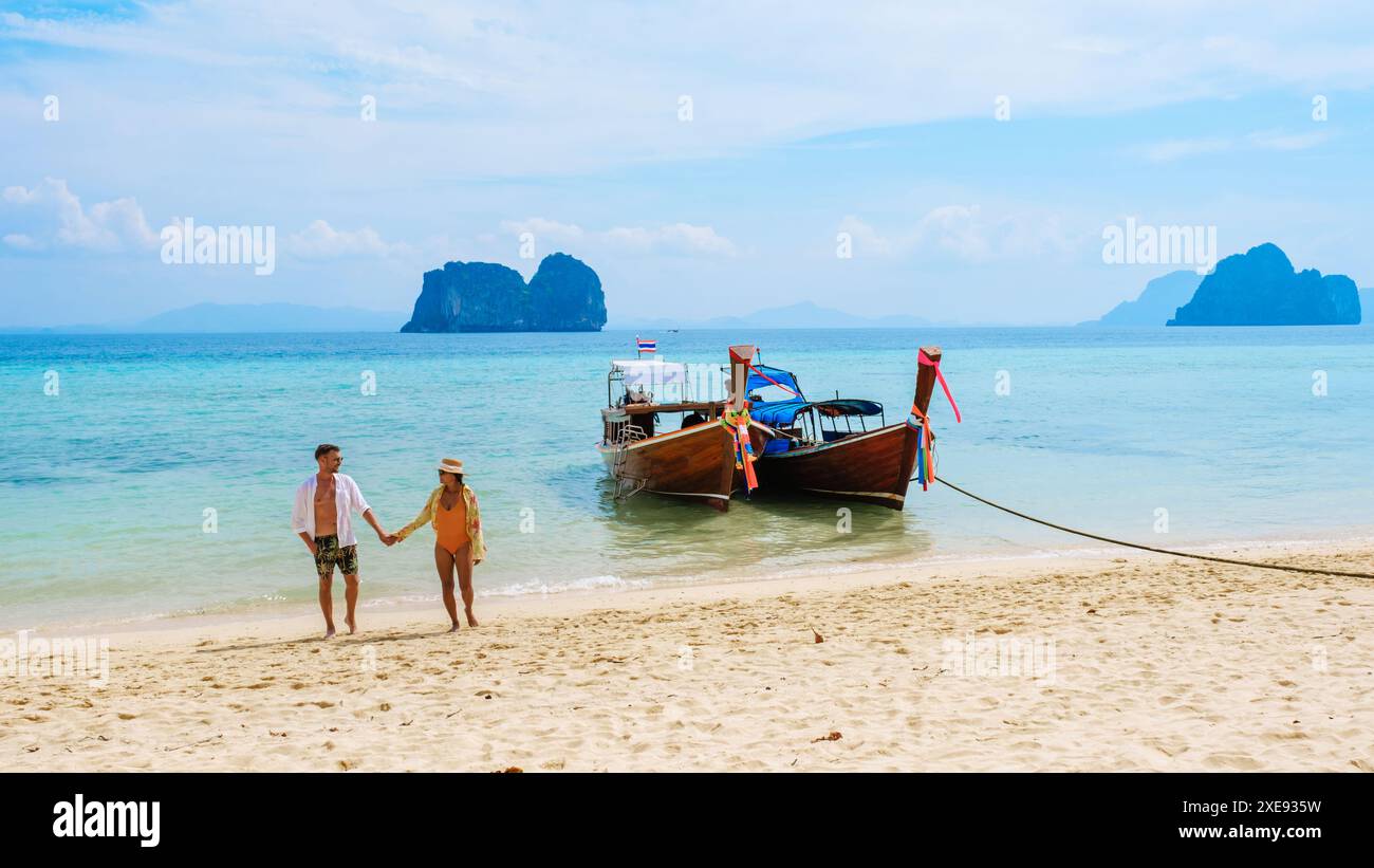 Ein paar Männer und Frauen laufen am Strand mit Longtail-Booten auf der Insel Koh Ngai Thailand Stockfoto