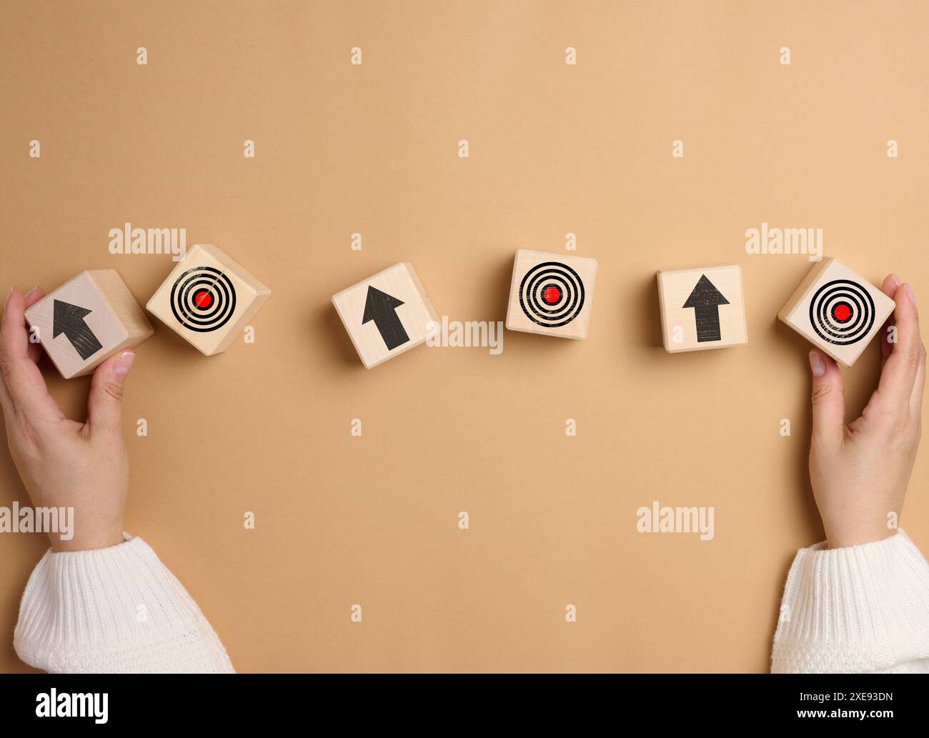 Die Hand einer Frau hält Holzwürfel mit Pfeilen und einem gezeichneten Ziel Stockfoto