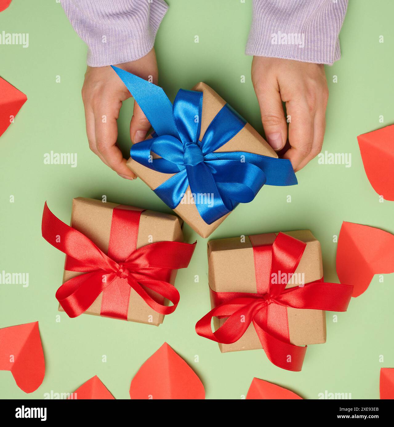 Frauenhand, die eine Geschenkbox in ein rotes Seidenband auf grünem Hintergrund hält, Ansicht von oben Stockfoto