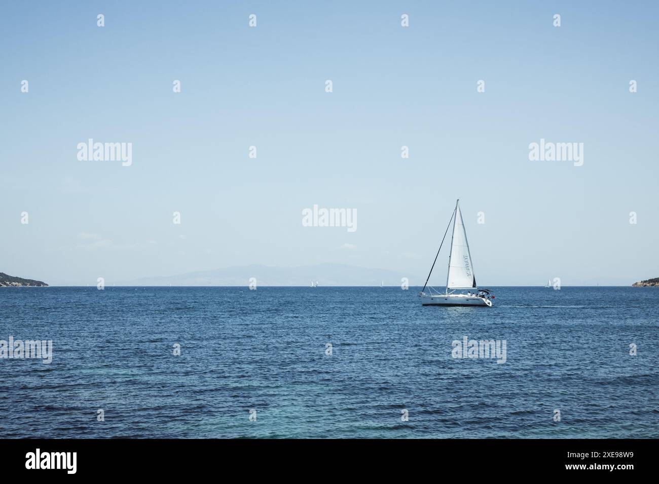 Ein einsames Segelboot auf dem blauen Meer in der Nähe der Küste in der wunderschönen türkischen Stadt Urla in der Nähe von Izmir in der Türkei an einem sonnigen Tag mit blauem wolkenlosem Himmel. Stockfoto