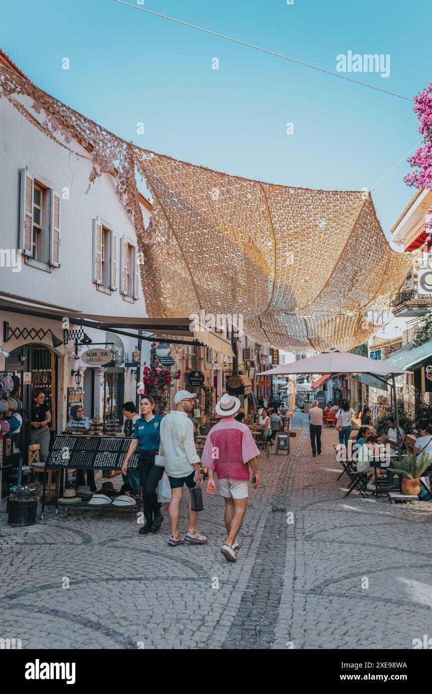 Menschen laufen die beliebte Straße Sanat Sokağı im Zentrum von Urla in der Nähe von Izmir an einem sonnigen Tag mit blauem Himmel und vielen Cafés, Bars und Restaurants entlang. Stockfoto