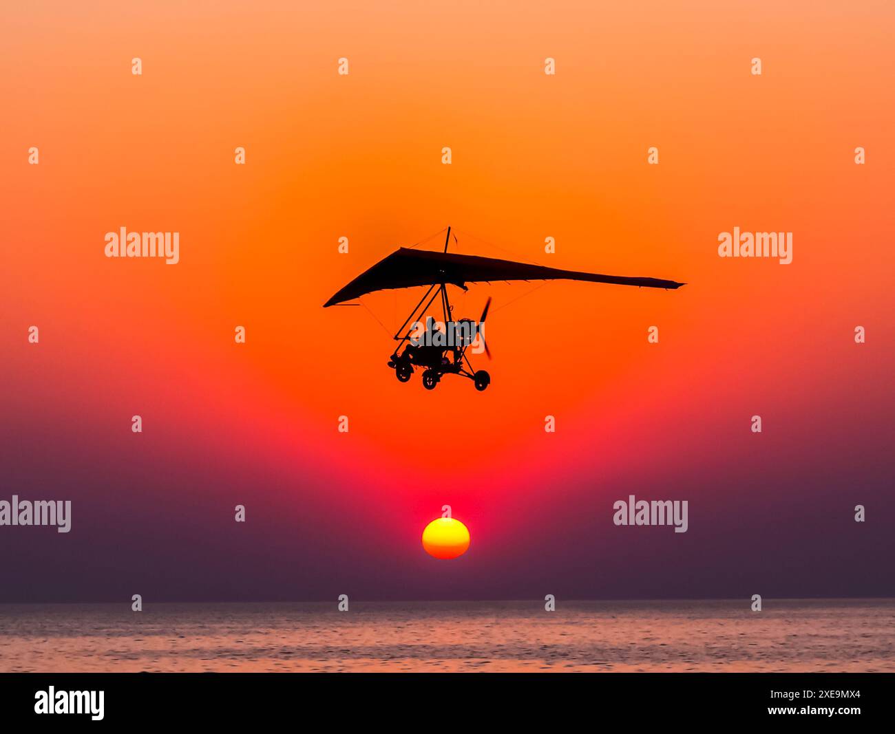 Motorisierter Segelflugzeug fliegt gegen den Sonnenuntergang über dem Meer. Stockfoto
