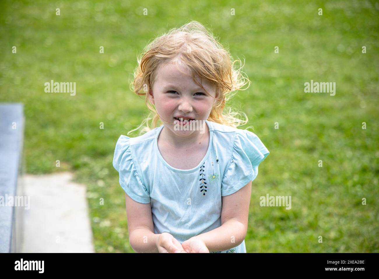 Ein kleines Mädchen trägt Wasser aus dem Brunnen der Stadt in Handvoll. Park Play-Konzept: Darstellung spielerischer Aktivitäten in Stadtparks. Stockfoto