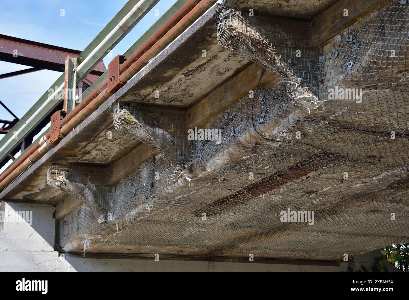Alte Betonbrückenkonstruktion stark beschädigt. Gefährliche Überführung. Drahtgeflecht hält die zerfallende Betonkonstruktion. Erosion auf Betonoberfläche. R Stockfoto