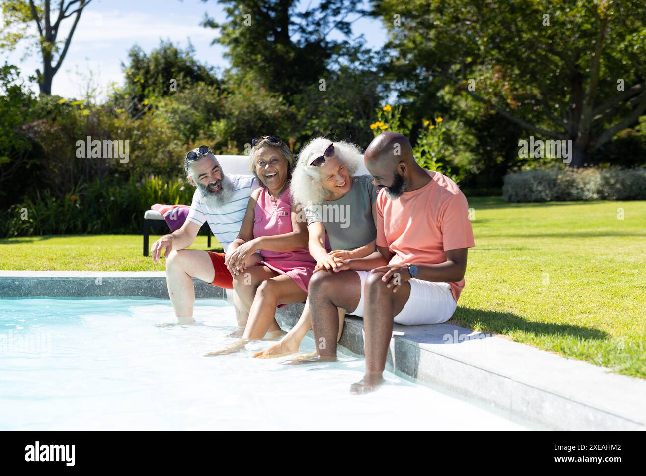 Eine Gruppe älterer Freunde sitzt am Pool, genießt den sonnigen Tag und lacht Stockfoto