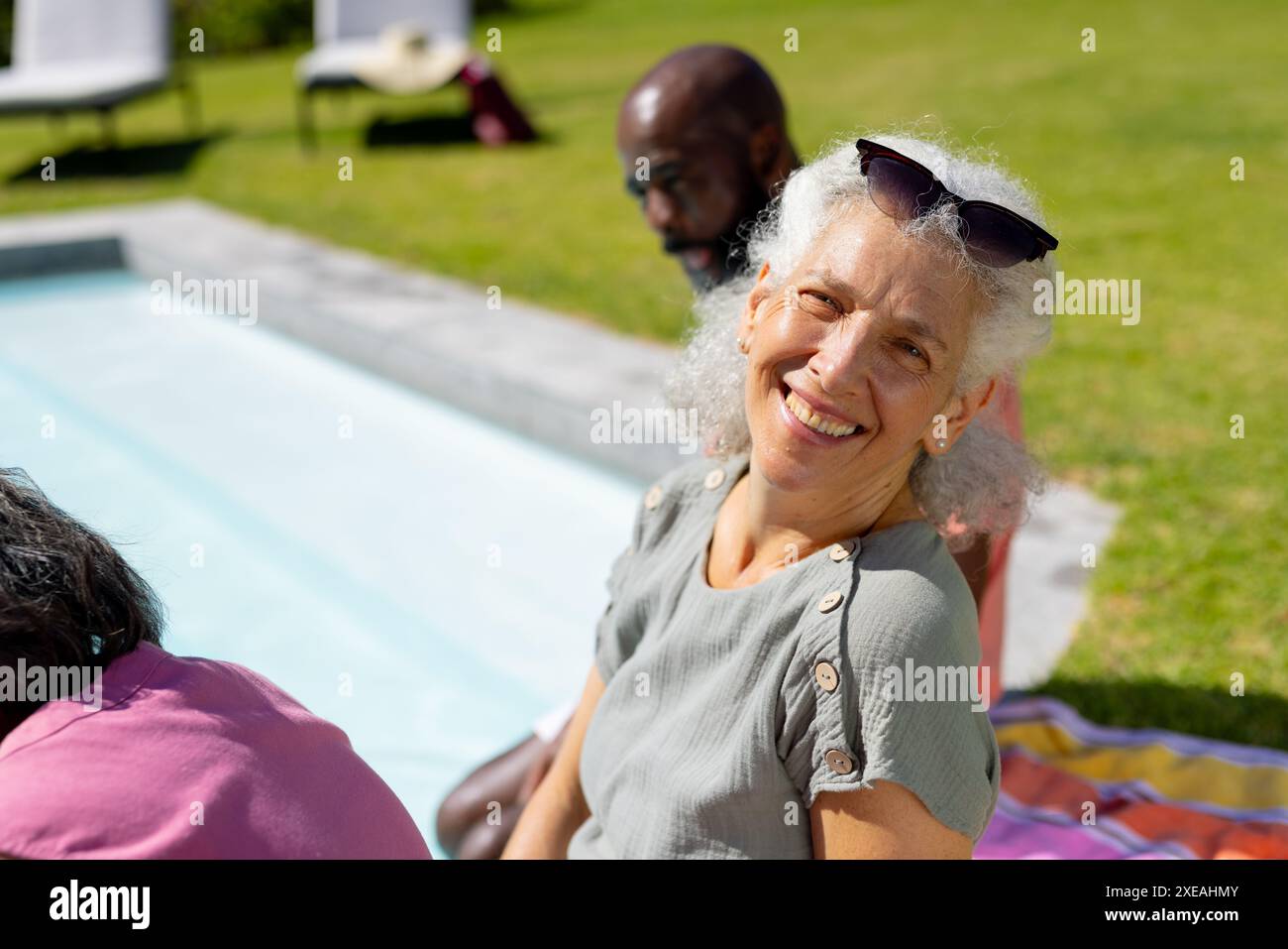 Lächelnde Seniorin, die sich am Pool mit Freunden am sonnigen Tag entspannt Stockfoto