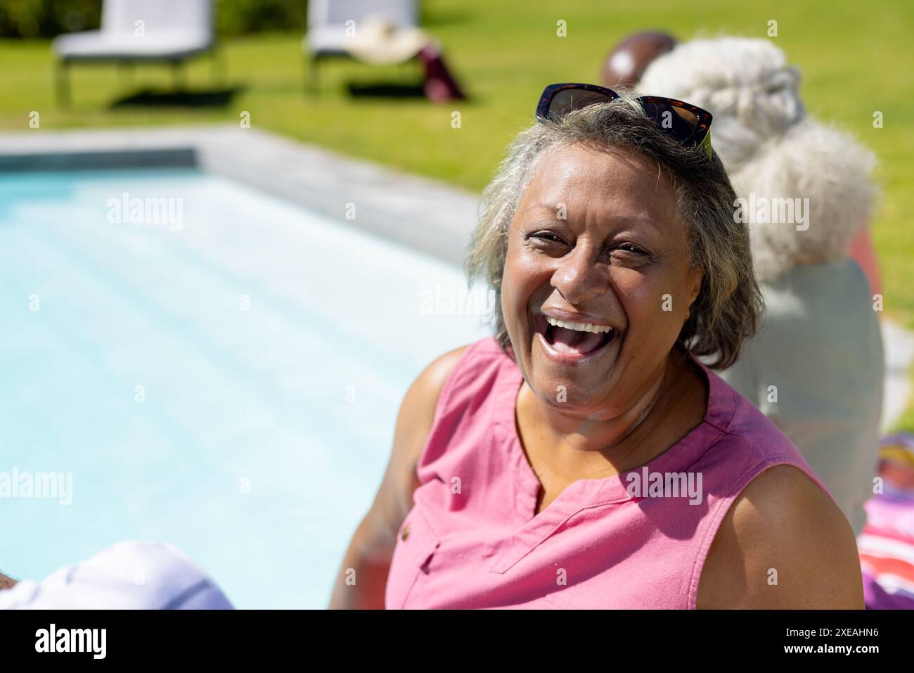 Lächelnde Seniorin genießt einen sonnigen Tag am Pool mit Freunden im Hintergrund Stockfoto