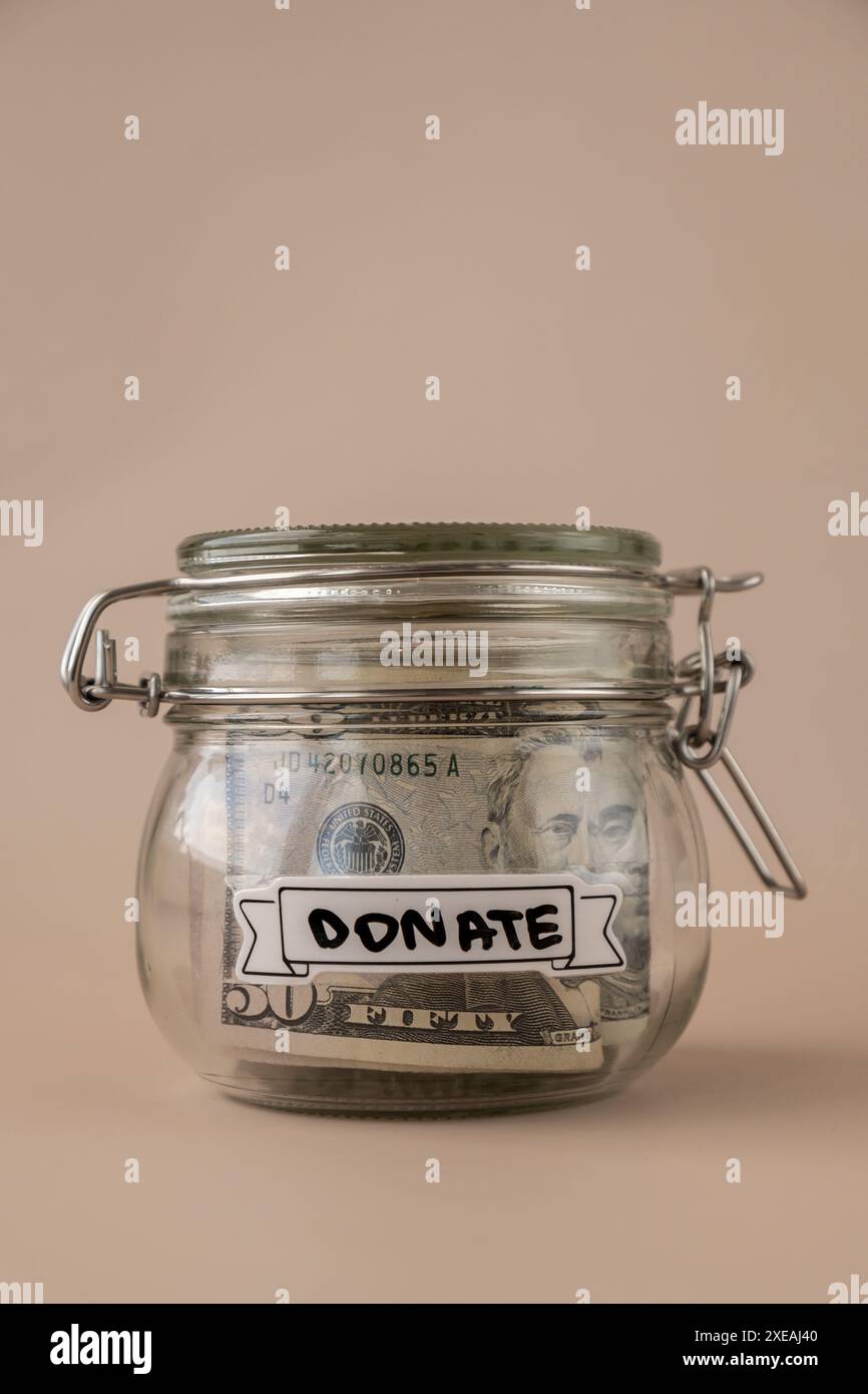 Sparen Sie Geld in einem Glasgefäß, gefüllt mit Dollarscheine. Transkription vor dem Gefäß SPENDEN. Persönliche Finanzen extra verwalten Stockfoto