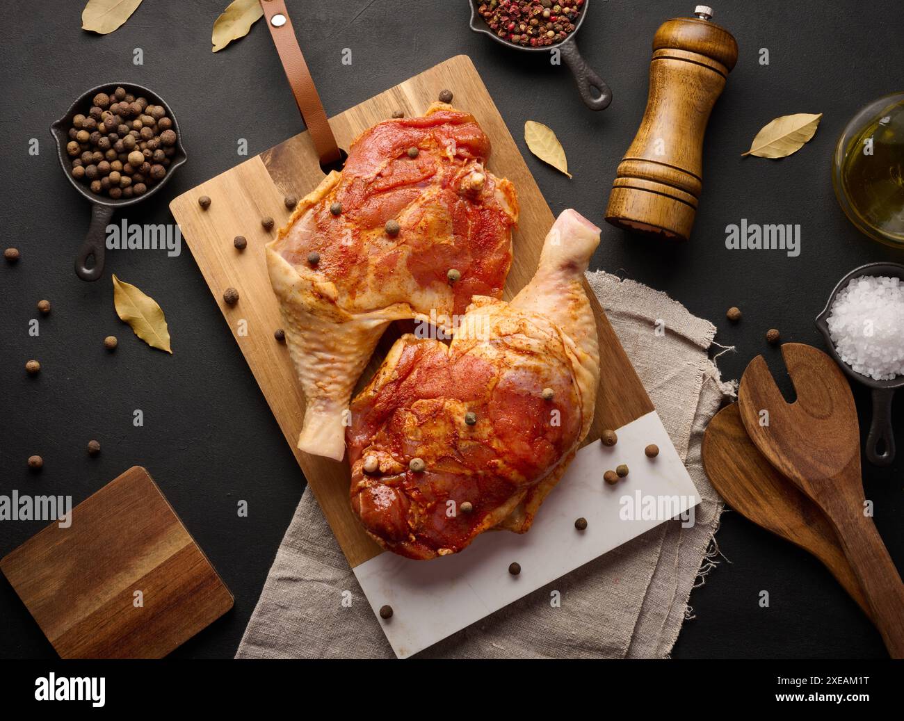 Rohe Hähnchenkeulen, gewürzt auf einem Holzbrett, begleitet von Salz und Pfeffer, von oben gesehen. Stockfoto