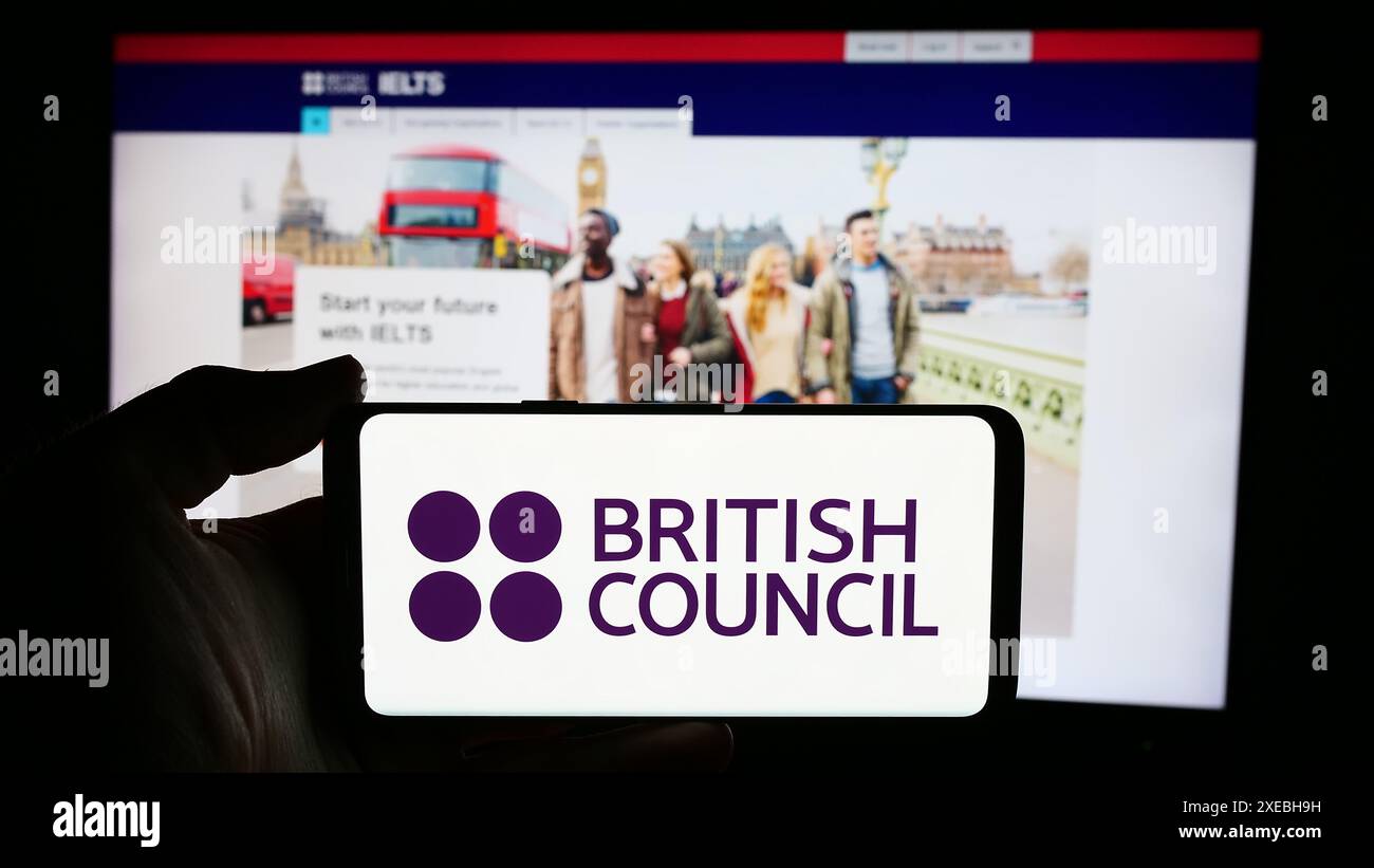 Person mit Handy mit Logo der Kultur- und Bildungsorganisation British Council vor der Webseite. Schwerpunkt auf dem Display des Telefons. Stockfoto