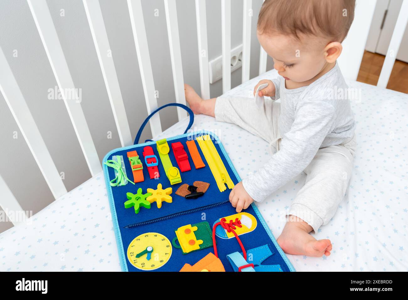 Baby spielt mit viel beschäftigtem Buch, das im Kinderbett sitzt. Konzept von Smart Books und modernem Spielzeug Stockfoto