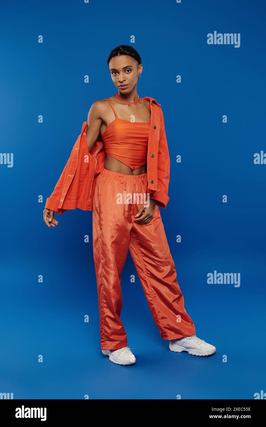 Eine hübsche junge Afroamerikanerin, die ein orangefarbenes Oberteil und eine Hose auf blauem Hintergrund trägt. Stockfoto