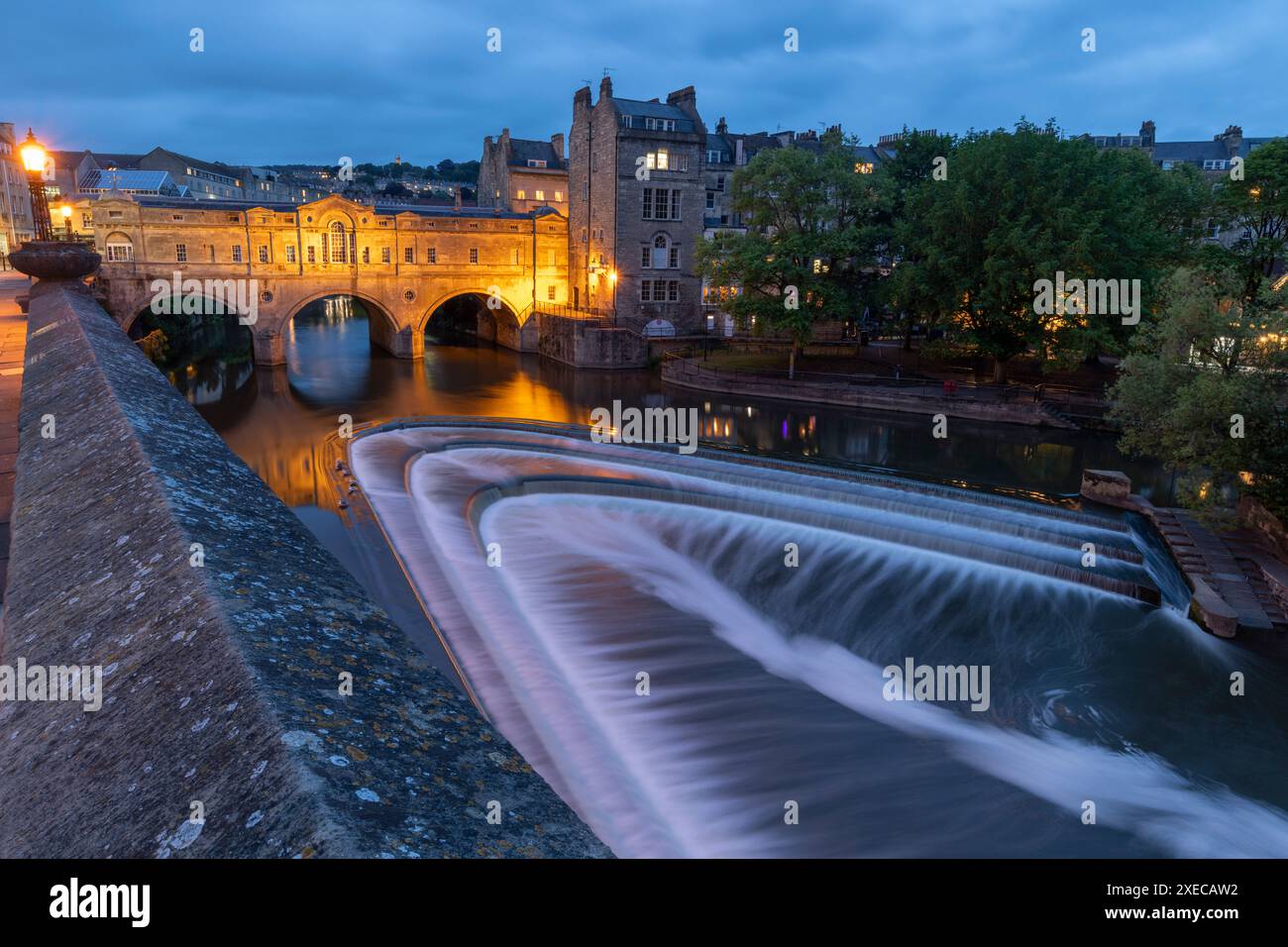 Pulteney Bridge und Wehr am Fluss Avon in der Abenddämmerung, Bath, Somerset, England. Sommer (Juni) 2019. Stockfoto