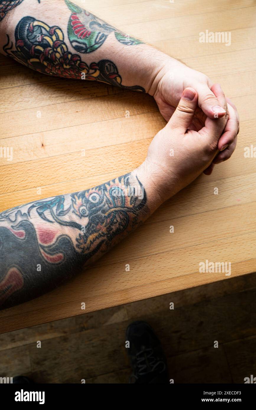 Tätowierte Arme auf einem Tisch in Cornwall in Großbritannien. Stockfoto