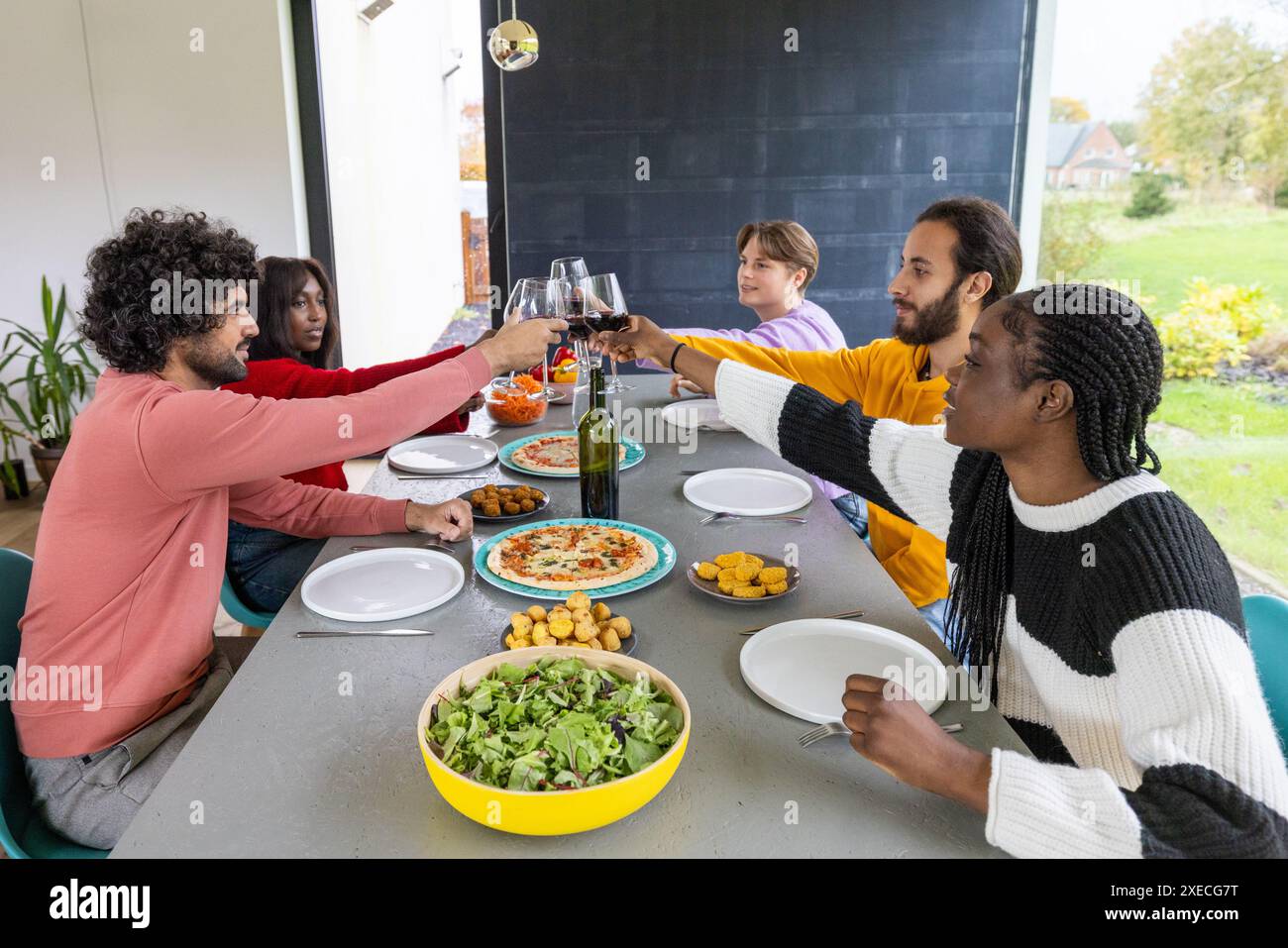 Fröhliches Essen: Freunde heben Gläser in einem gemeinsamen Essen zu Hause Stockfoto