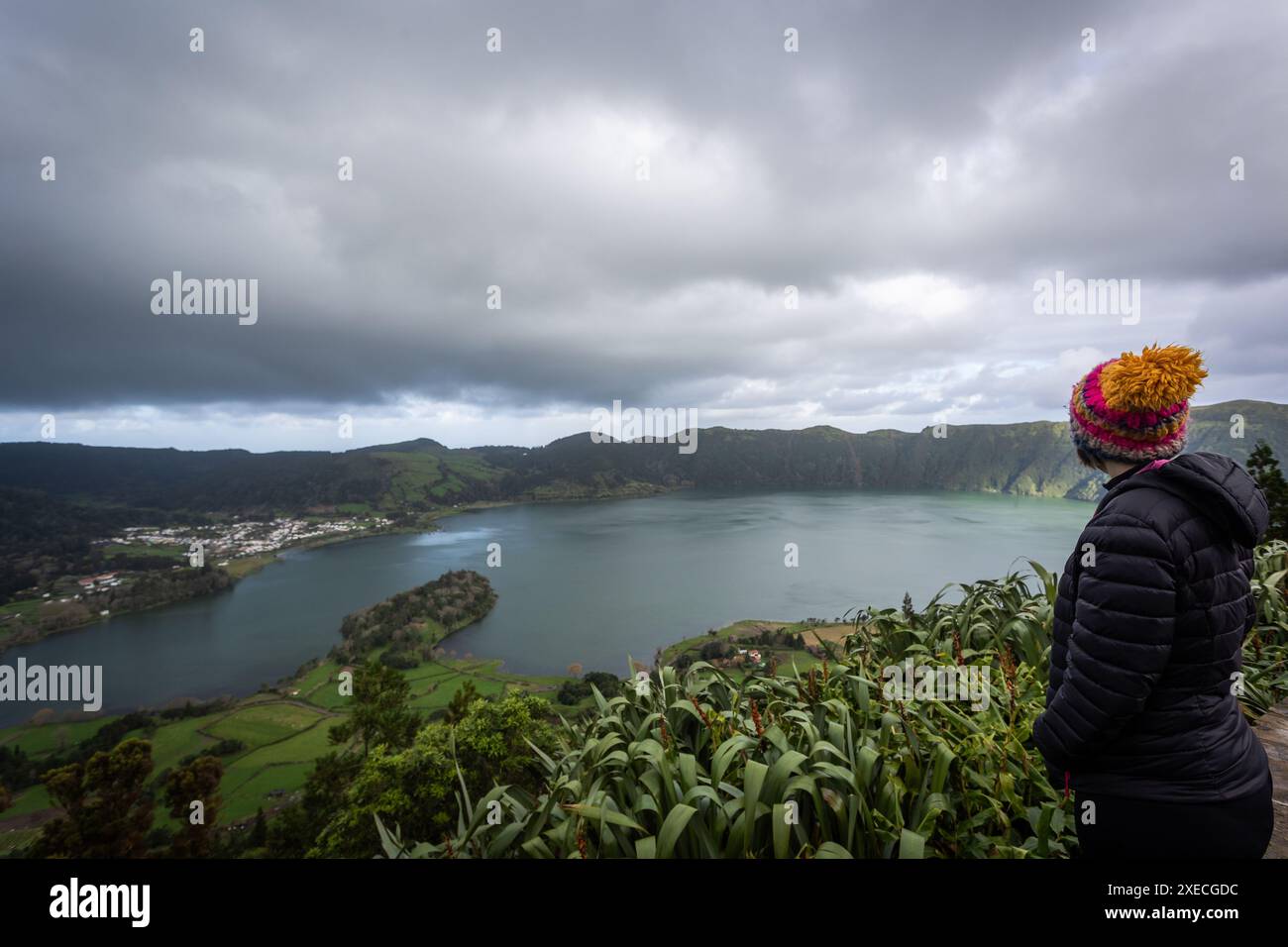 Eine Frau mit farbenfroher Mütze und schwarzer Jacke blickt über den malerischen See Sete Cidades auf der Insel São Miguel auf den Azoren. Der ruhige See, s Stockfoto