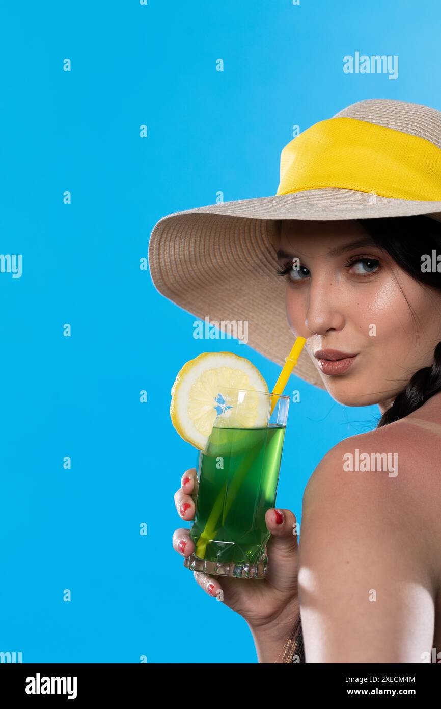 Ein Teenager mit einem alkoholischen Getränk in der Hand und einem großen Hut sonnt sich in der Sommersonne. Stockfoto