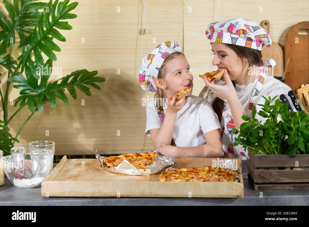 Die fünfjährige Tochter setzte sich auf den Schoß ihrer Mutter und zusammen essen sie selbst gebackene Pizza. Nach der Arbeit Stockfoto