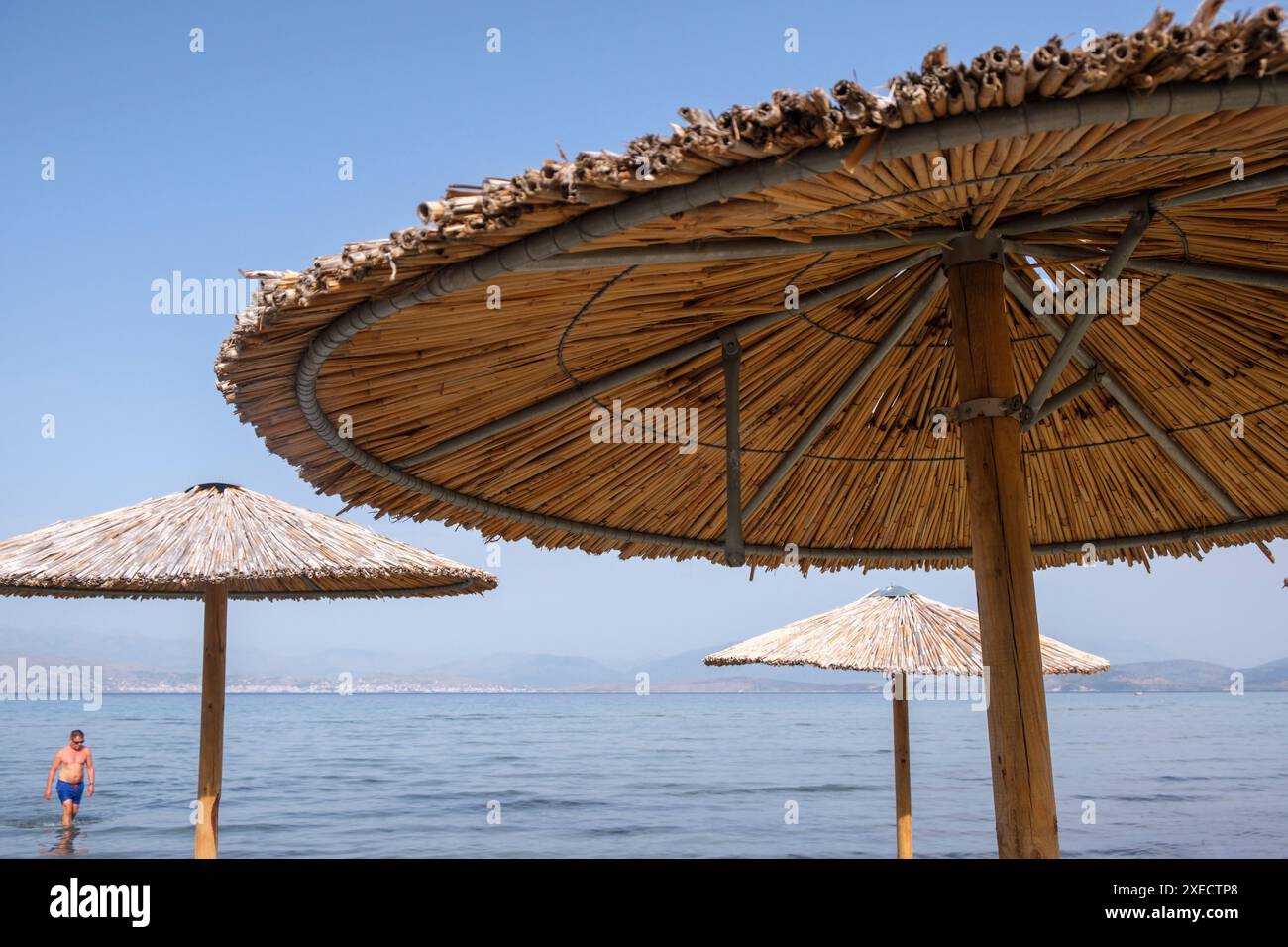 Großer Schilfschirm an einem Strand auf Korfu in Griechenland, mit ruhigem tiefblauem Meer. Stockfoto