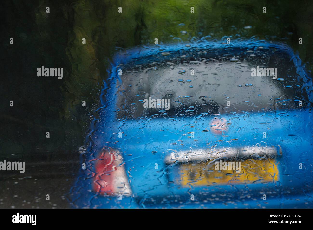 Ein leeres blaues Auto parkt am Straßenrand, durch eine regenbedeckte Windschutzscheibe gesehen. Stockfoto