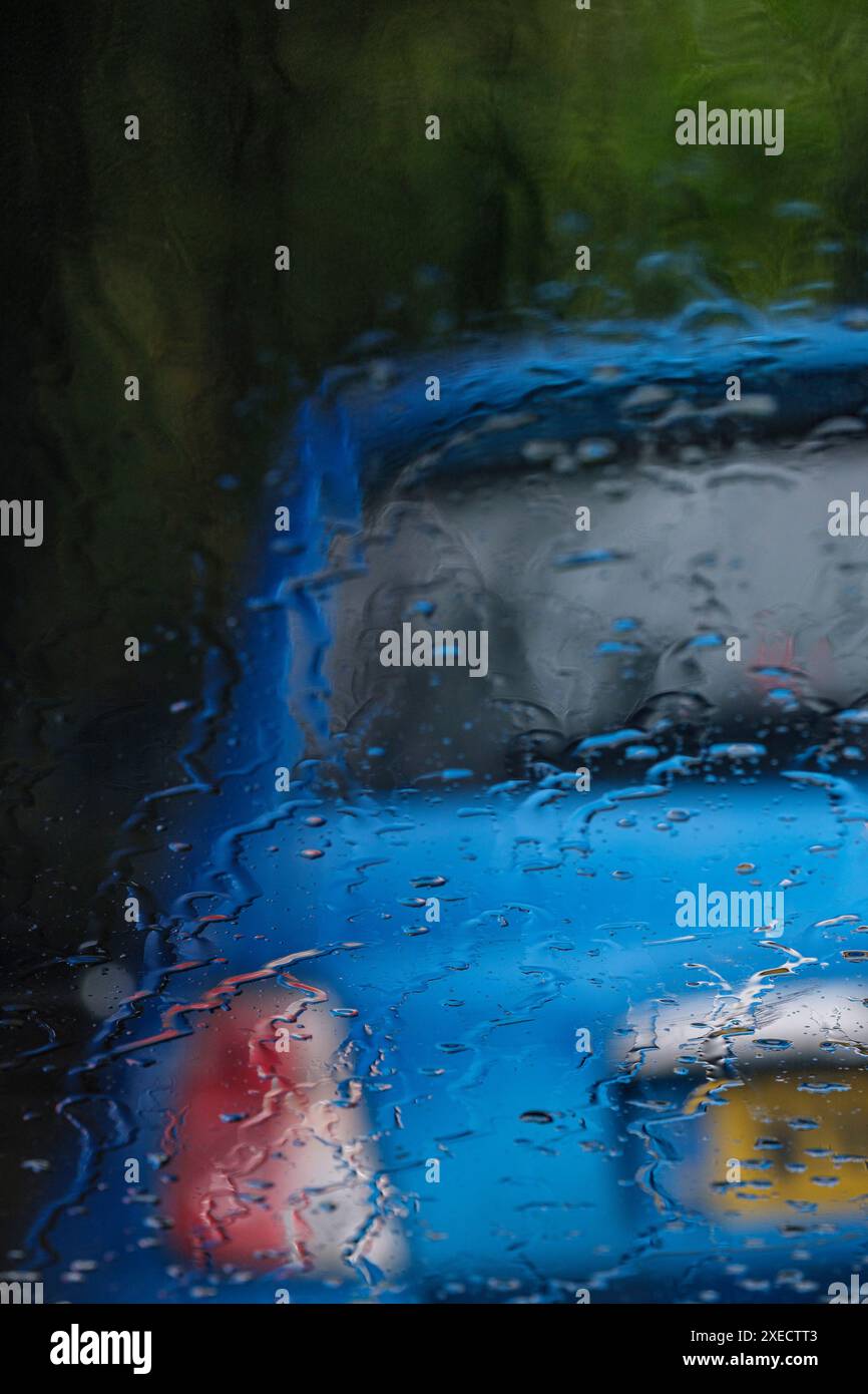 Ein leeres blaues Auto parkt am Straßenrand, durch eine regenbedeckte Windschutzscheibe gesehen. Stockfoto