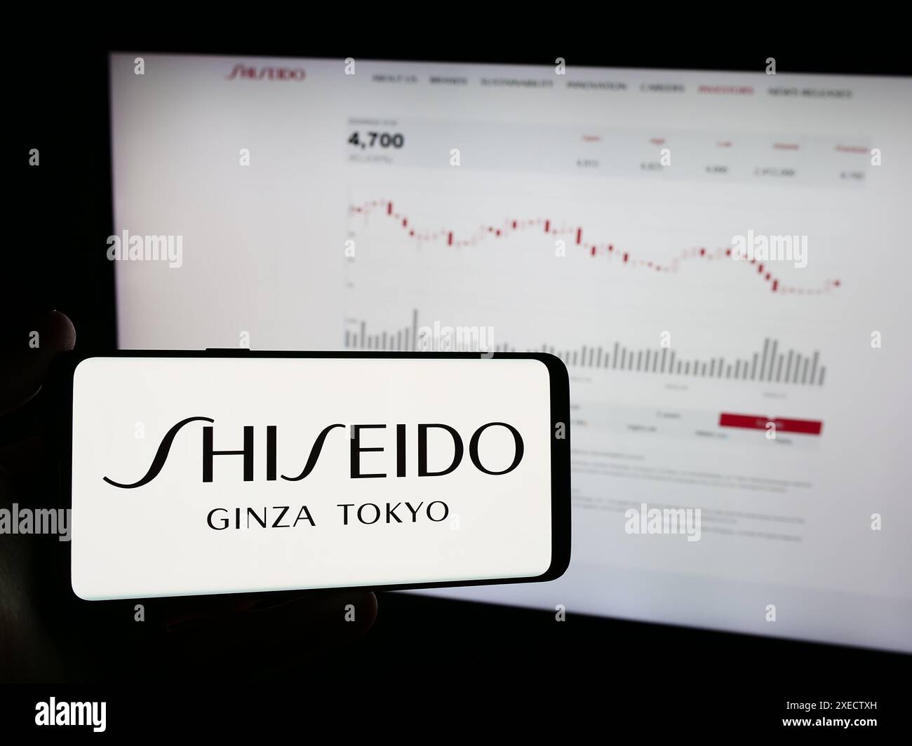 Person, die ein Mobiltelefon mit dem Logo des japanischen Kosmetikunternehmens Shiseido Co. Ltd. Vor der Business-Webseite hält. Schwerpunkt auf dem Display des Telefons. Stockfoto