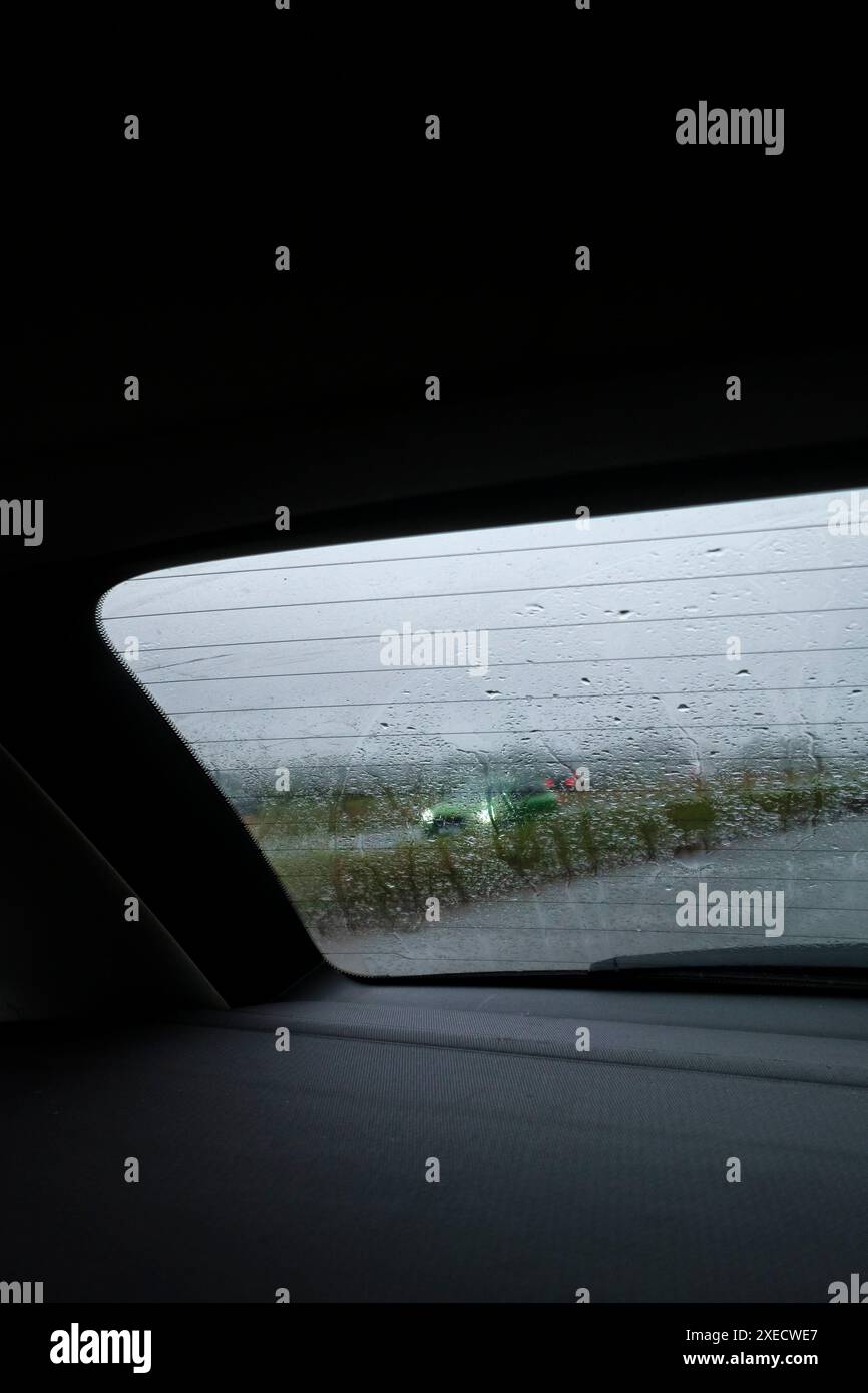 Blick durch die regenbedeckte Heckscheibe eines Autos, während der Verkehr vorbeifährt. Stockfoto
