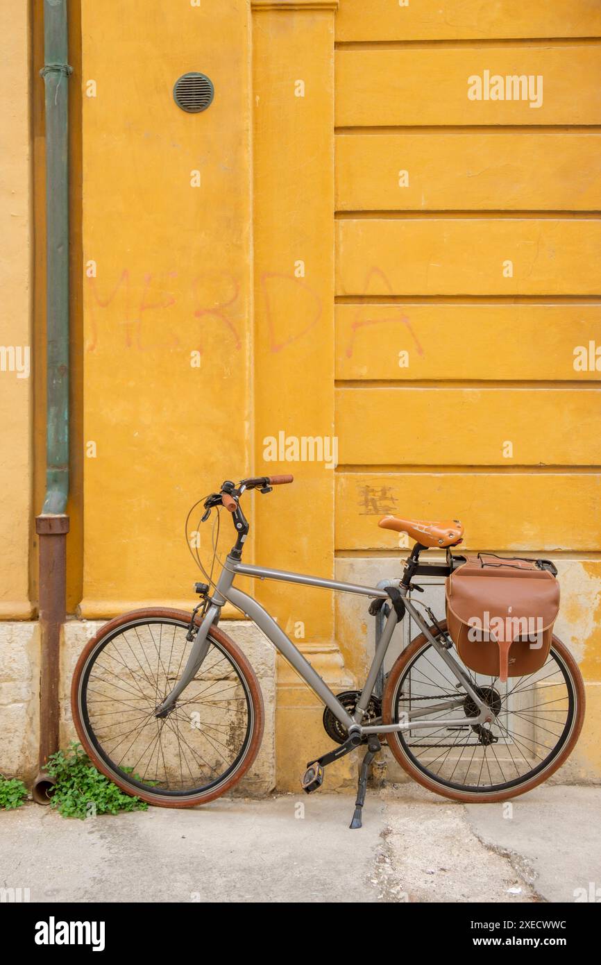 Ein Tretrad, das in einer italienischen Stadt vor einer tieffarbigen gelben Wand steht. Stockfoto