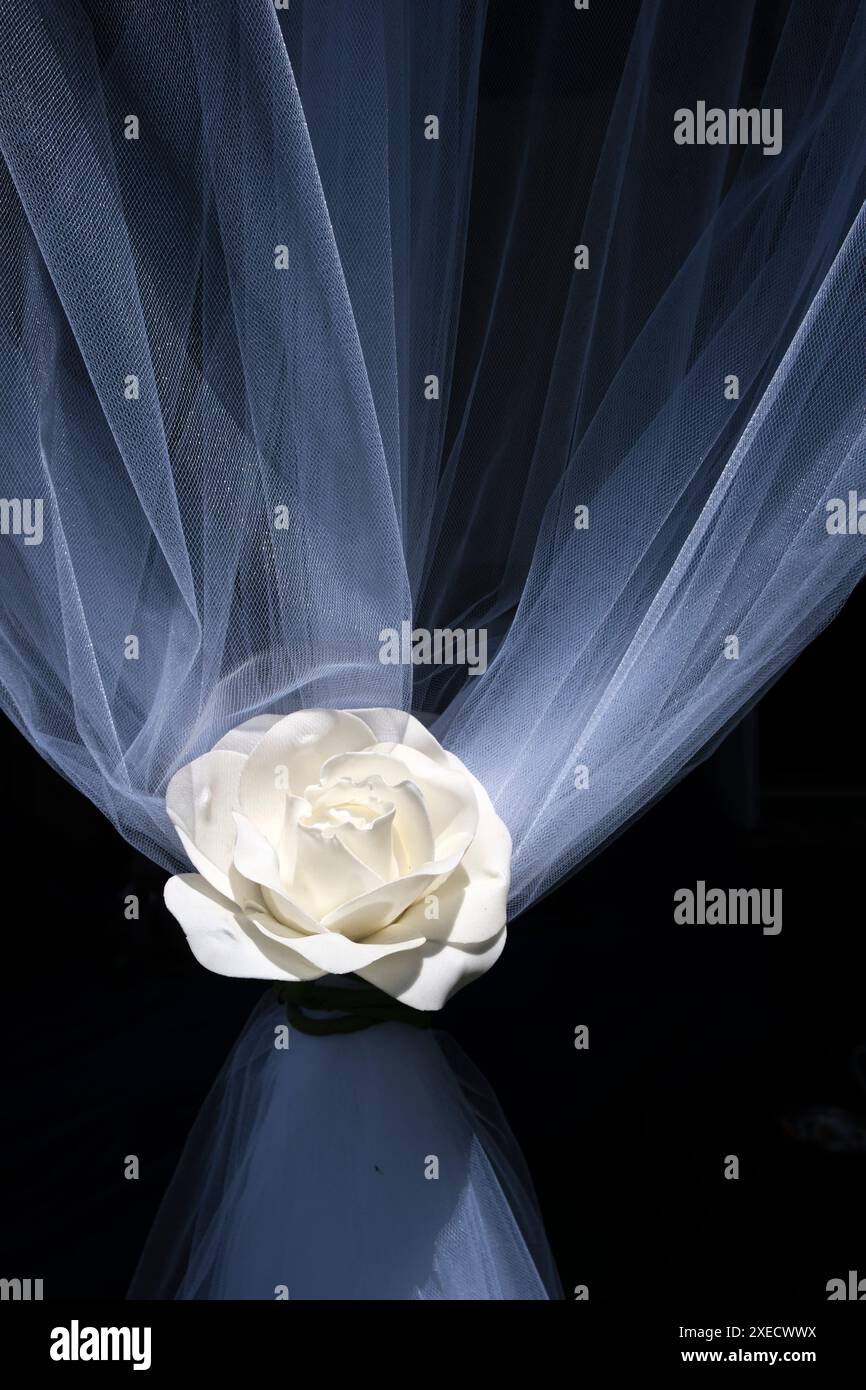 Eine weiße künstliche Rose, die an einen feinen Netzvorhang gebunden ist, auf einer Hochzeitsfeier. Stockfoto