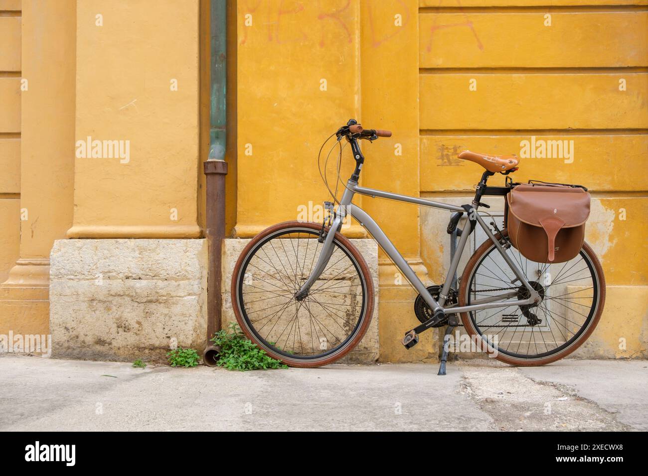 Ein Tretrad, das in einer italienischen Stadt vor einer tieffarbigen gelben Wand steht. Stockfoto