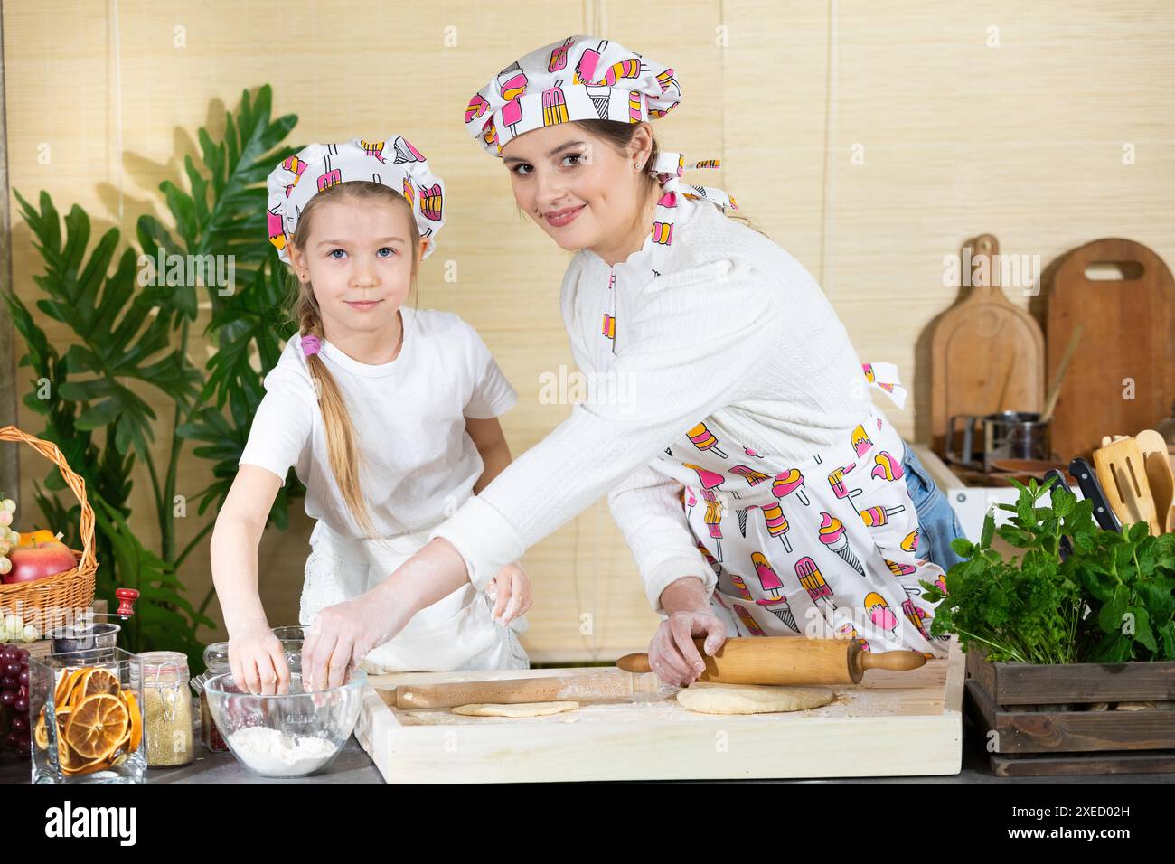 Eine hübsche Mutter und eine fünfjährige Tochter greifen zusammen nach frischem Weizenmehl, um sich die Hände darin zu bekleiden und darüber zu streuen Stockfoto