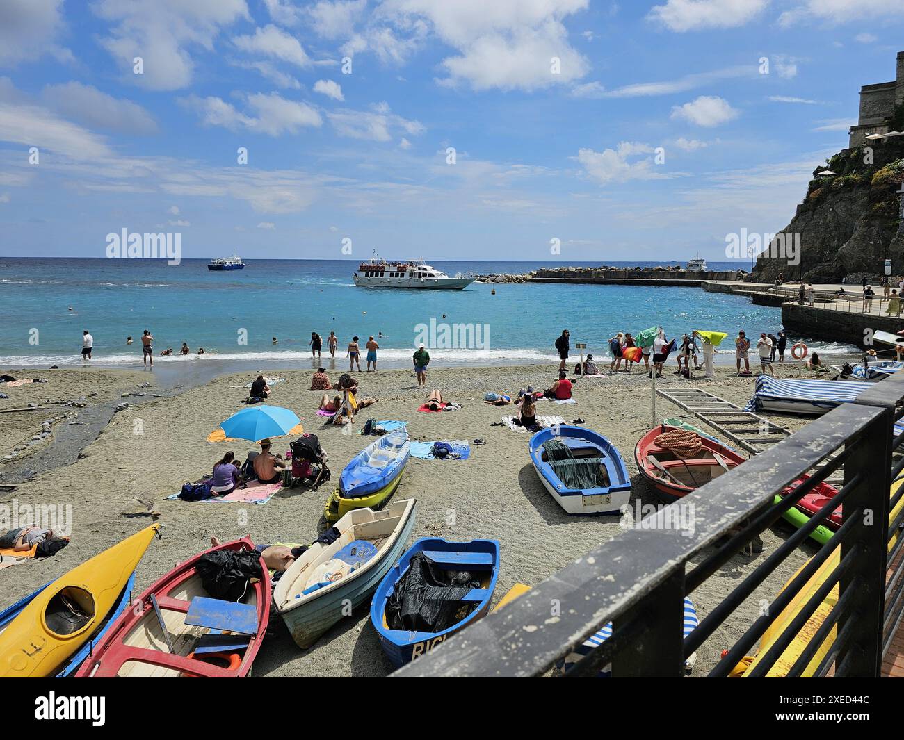 Nicht erkennbare Touristen, die am Sandstrand zwischen Ruderbooten rumhängen. Menschen schwimmen und sonnen sich. Stockfoto