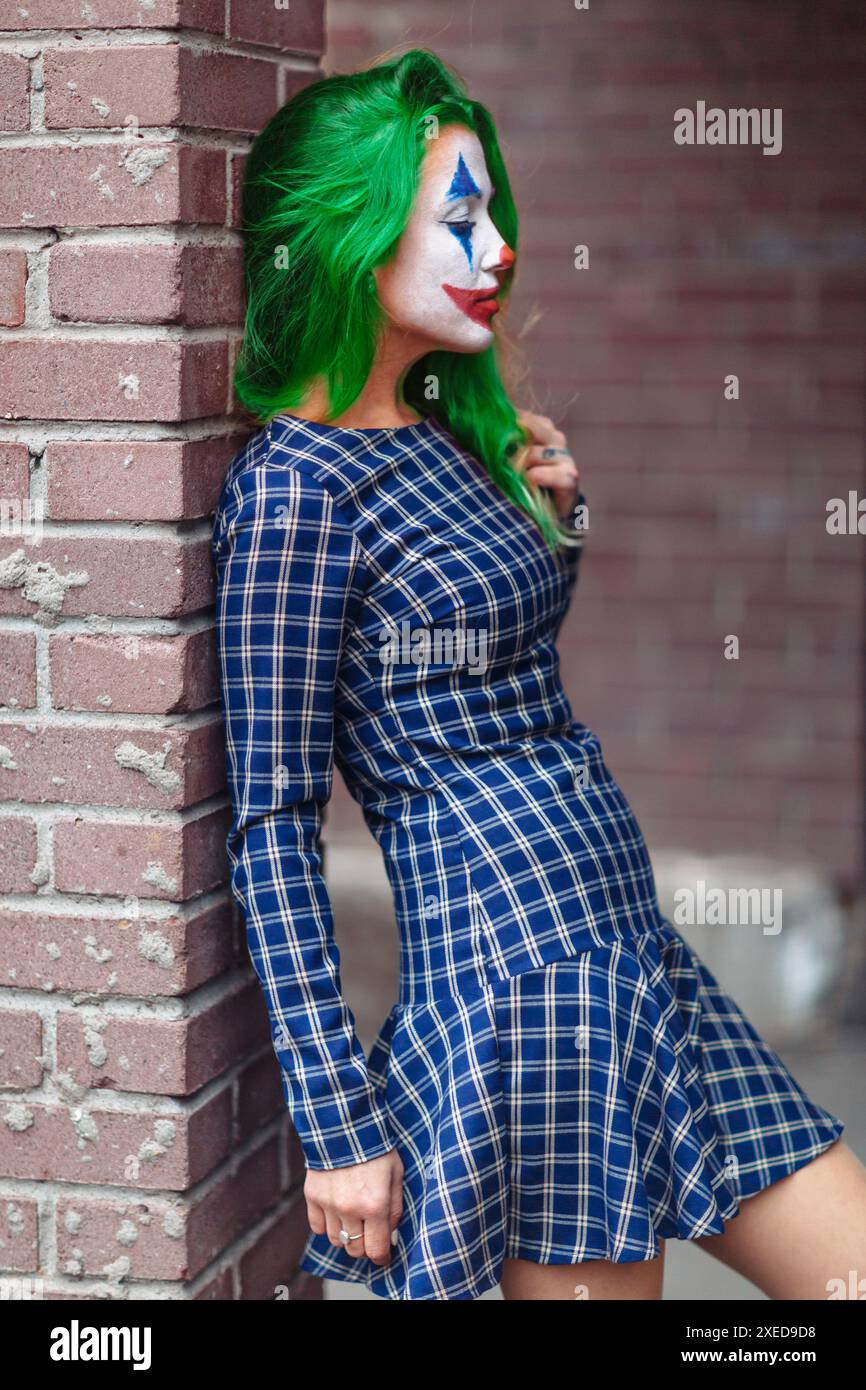 Porträt eines grünhaarigen Mädchen in gechert Kleid mit Joker Make-up auf einer Ziegelwand verschwommen Hintergrund. Stockfoto