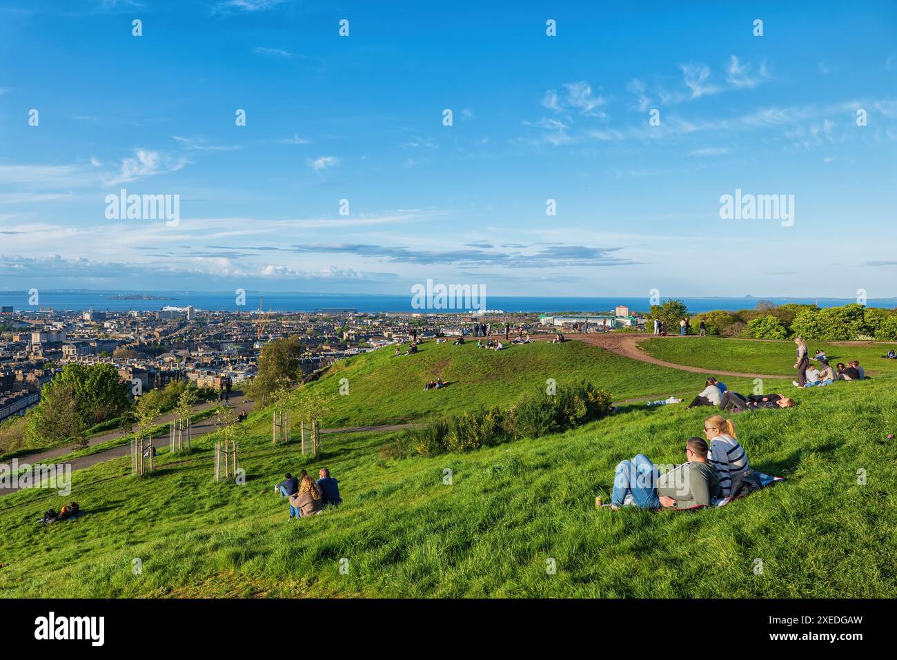 Die Menschen sitzen und liegen auf dem Gras am Calton Hill im Frühjahr, der Stadt Edinburgh in Schottland, Großbritannien. Stockfoto