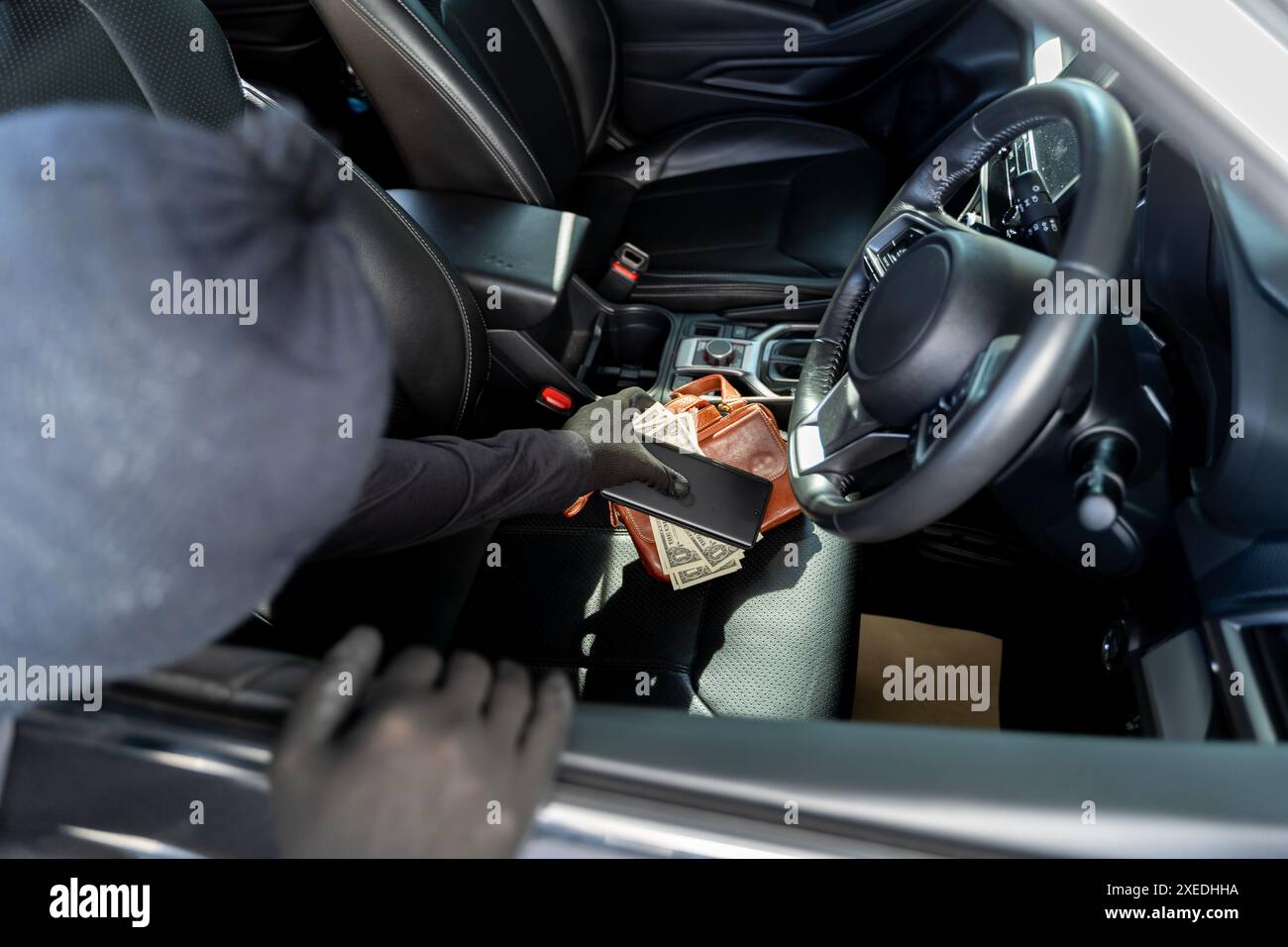 Eine Hand, die eine Brieftasche vom Beifahrersitz eines Autos zieht. Wertvolle persönliche Dinge, die auf dem Vordersitz liegen, sind für Diebe leicht auffangen. Thiev Stockfoto