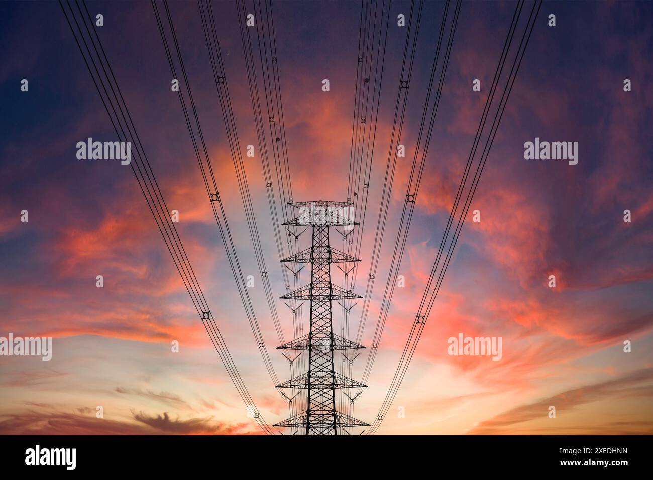 Eine Stromleitung durchquert den Vordergrund eines dramatischen Sonnenuntergangs. Die untergehende Sonne wirft ein warmes Licht über die Landschaft und bildet die Silhouette der Stromleitung und ihrer Su Stockfoto