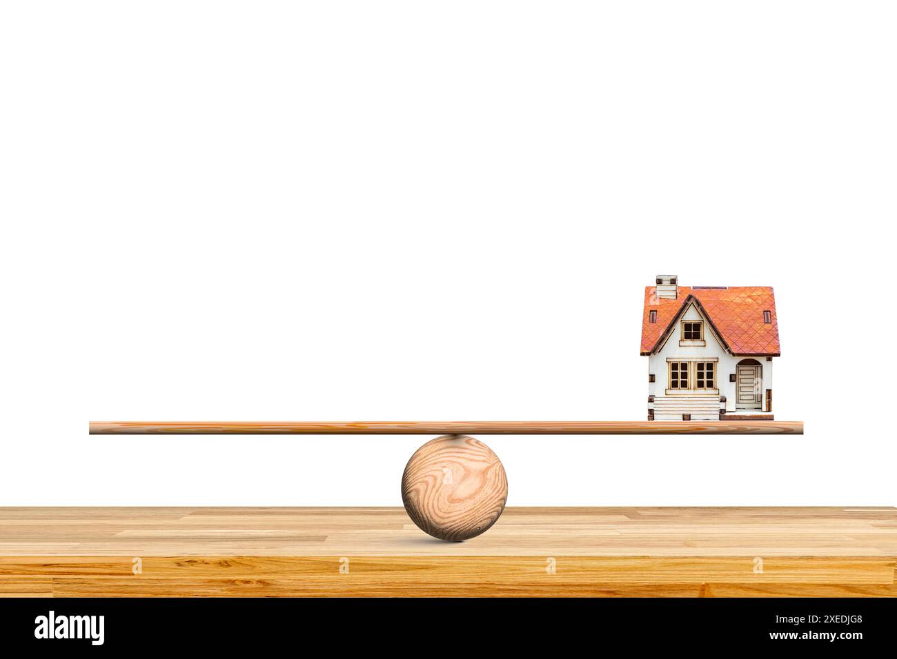 Weißes Haus mit rotem Dach. Das Haus sitzt auf einer hölzernen Wippe, die auf einem Holztisch ausgeglichen ist. Geschäftskonzept für Finanzimmobilien Stockfoto