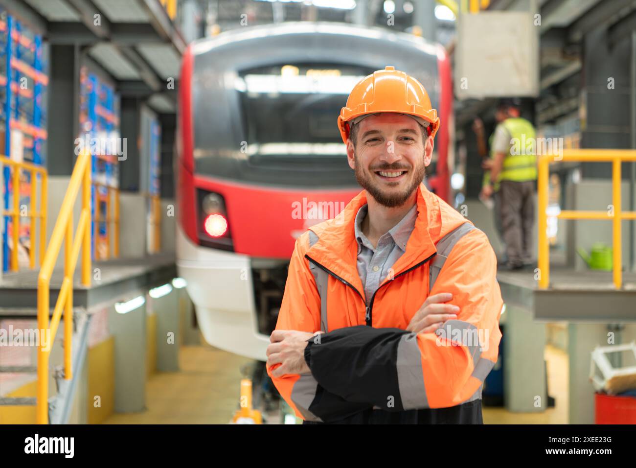 Porträt eines jungen männlichen Technikers, der vor dem Kopf von elektrischen Zügen in der Skytrain-Reparaturstation steht Stockfoto