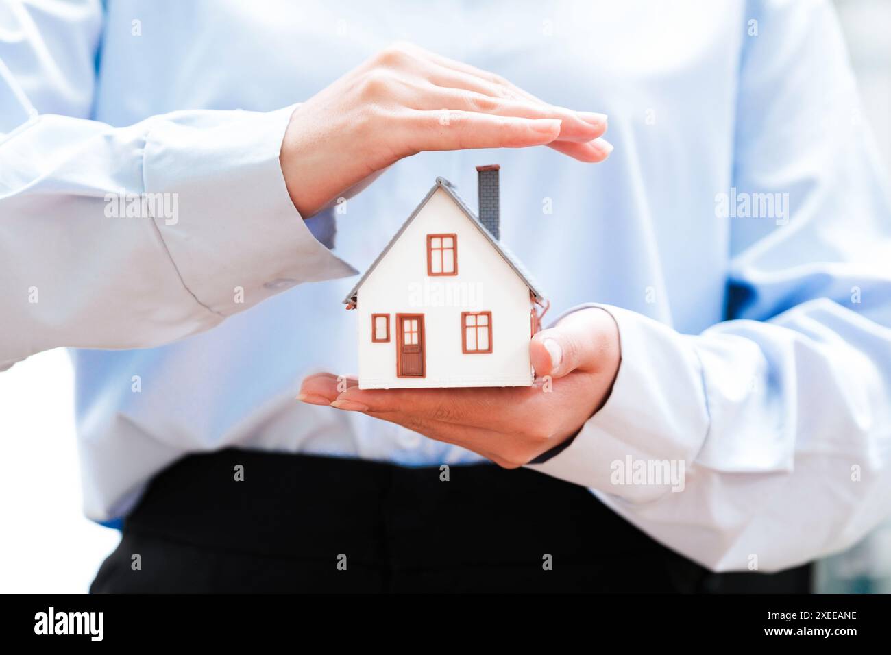 Hände, die ein kleines Hausmodell halten und die Sicherheit im Hausbesitz darstellen. Stockfoto