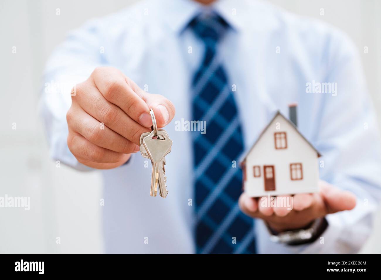 Der Immobilienmakler bietet Hausschlüssel und Modellhaus an, was den erfolgreichen Besitz veranschaulicht. Stockfoto