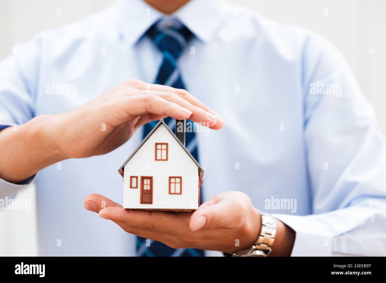 Hände, die ein kleines Hausmodell halten und die Sicherheit im Hausbesitz darstellen. Stockfoto
